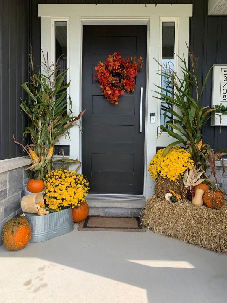 A front porch decorated with mums, pumpkins, corn stalks and straw bales